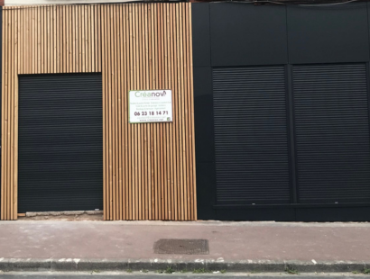 Photographie de volets roulants sur une porte d'entrée ainsi que des fenêtres, la façade est en bardage bois et aluminium